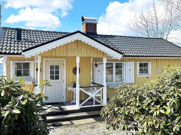 Ein gelbes Holzhaus mit weißem Veranda, Schornstein und einem kleinen Garten mit Pflanzen.