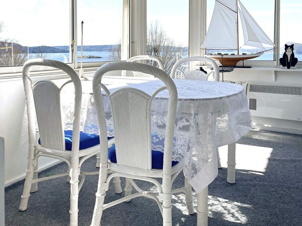 A room with a table and chairs, a sailboat model, and a view of a lake through large windows.