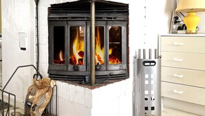 A wood-burning stove with visible flames, a metal ash collector, and a bag of firewood. - 4 Star Holiday Home in Uddevalla (Uddevalla)