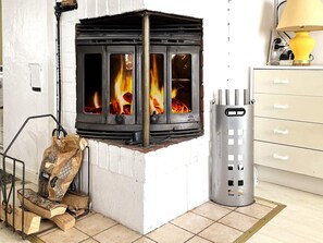 A wood-burning stove with visible flames, a metal ash collector, and a bag of firewood.