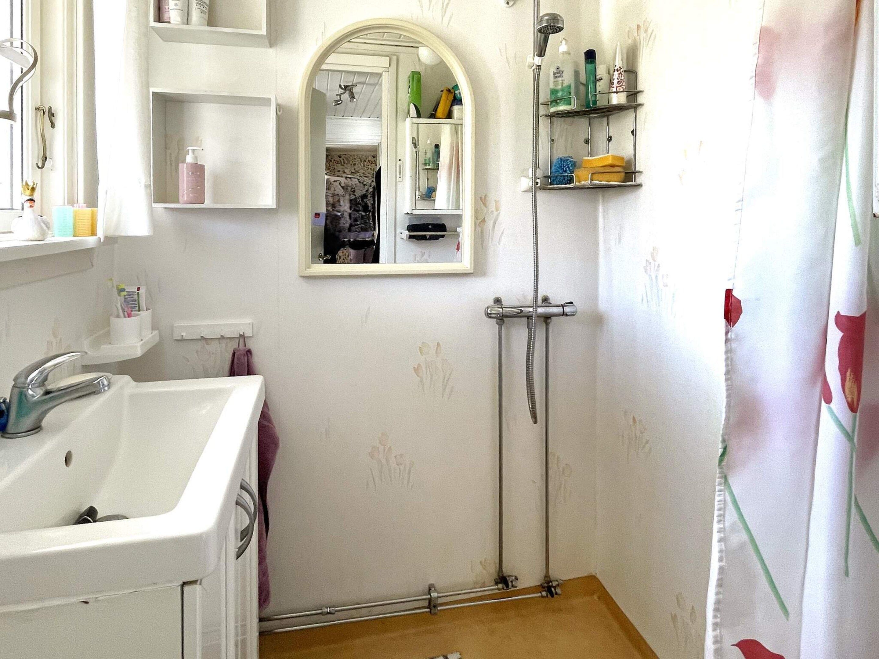 Une salle de bain équipée d’un lavabo, d’un miroir, d’une douche et d’étagères où sont rangés les articles de toilette.