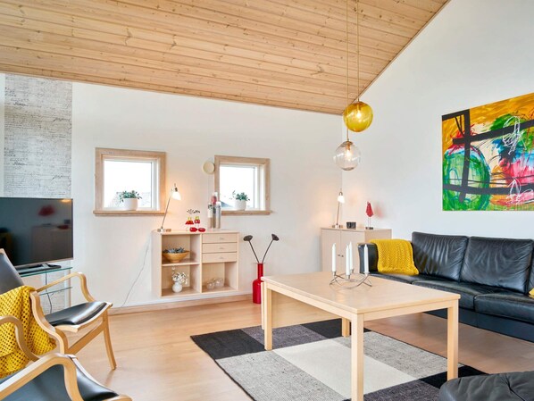 A modern living room with a wooden ceiling, a black leather sofa, a wooden coffee table, and a colorful abstract painting on the wall. - 5 Star Holiday Home in Allinge (Allinge)