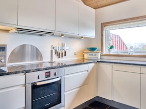 A modern kitchen with white cabinetry, a stainless steel oven, and a window with a view of a red building. - 5 Star Holiday Home in Allinge (Allinge)