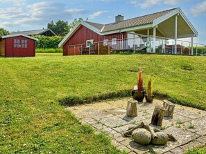 Une maison en bois rouge, dotée d’un porche et d’un champ verdoyant devant.
