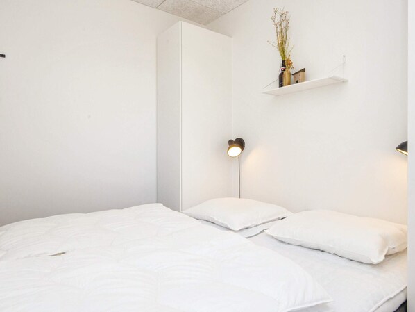 A minimalist bedroom with a bed, bedside lamps, and a shelf with a vase. - 5 Star Holiday Home in Romo (Rømø)