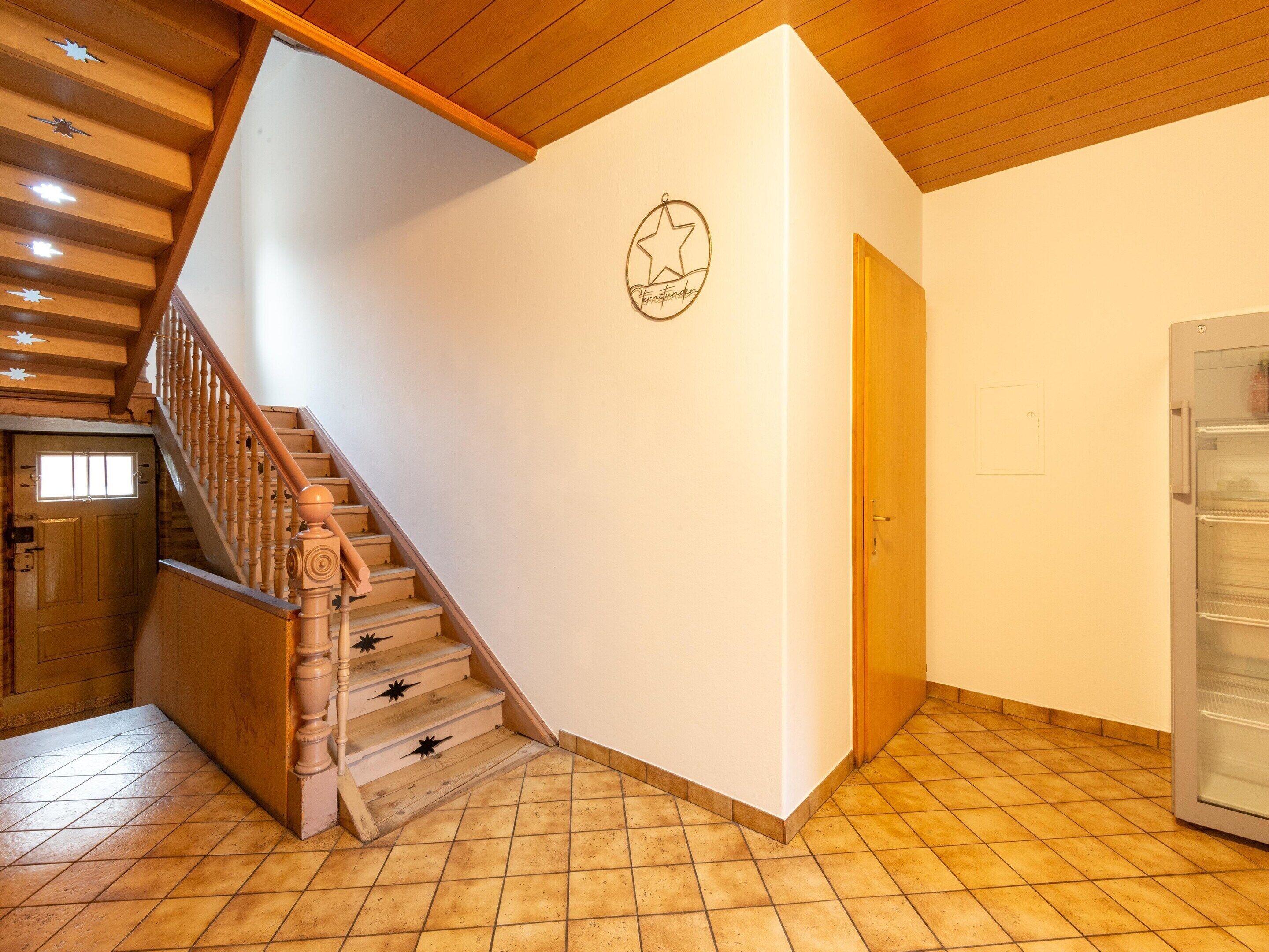 A staircase with wooden railings leading to a landing. A door with a star logo is visible on the landing wall.