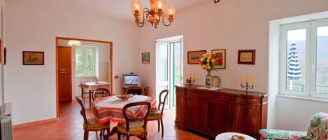 A dining area with a table and chairs, a television, a cabinet, and a window with a view.