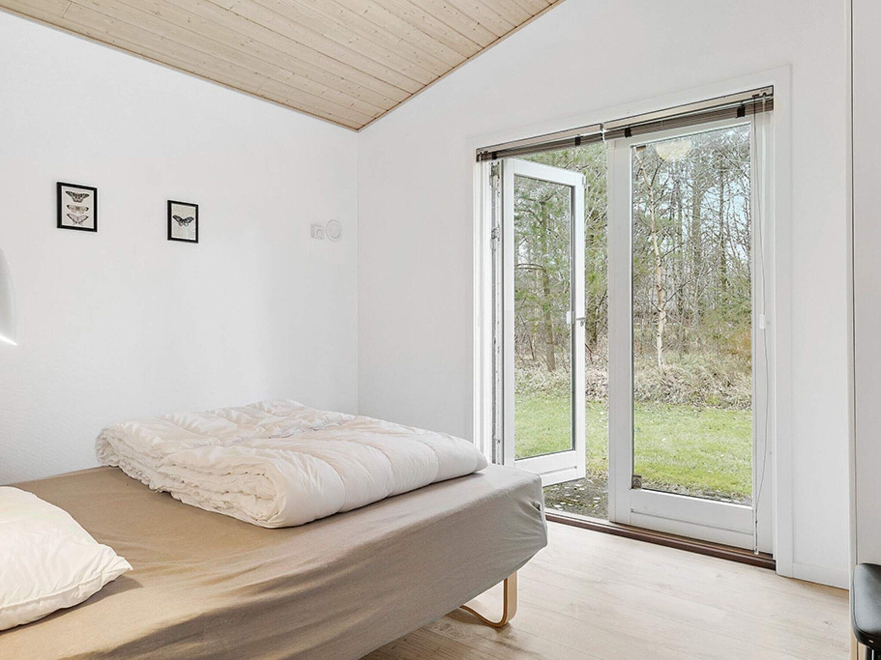 A bedroom with a bed, a large window, and a view of the outdoors.
