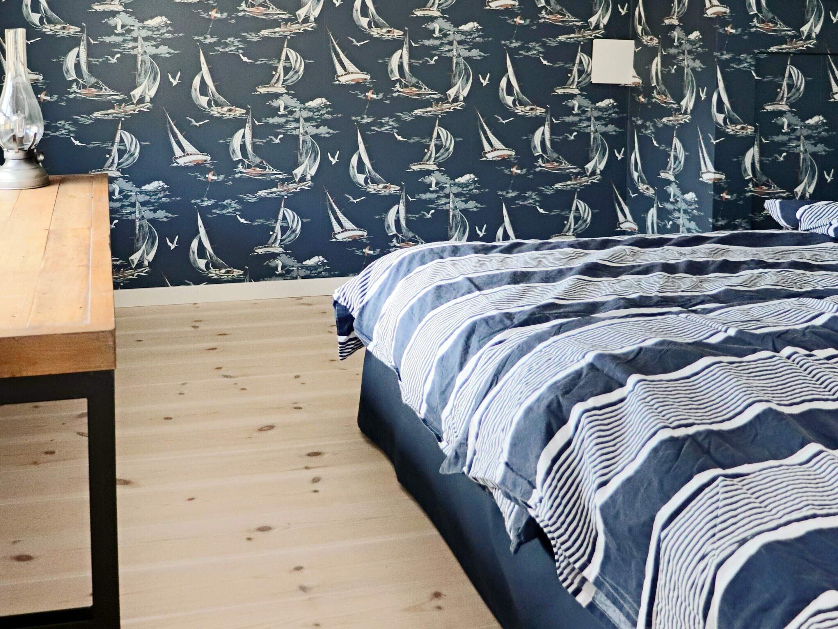 Une pièce comprenant un lit, une table en bois et un mur orné d’un motif représentant un voilier.