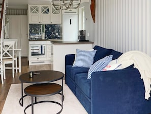 A living room with a blue sofa, striped pillows, a round coffee table, and a kitchen area in the background. - 4 Star Holiday Home in Varberg (Varberg)