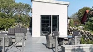 A modern outdoor seating area with wicker furniture, a stone wall, and a clear sky. - 4 Star Holiday Home in Varberg (Varberg)