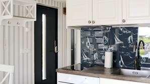 Una cucina con mobili bianchi, una porta nera e un pannello decorato con disegni di barche a vela.