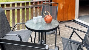Una mesa redonda de vidrio con dos tazas blancas y una tetera anaranjada sobre una terraza de madera.