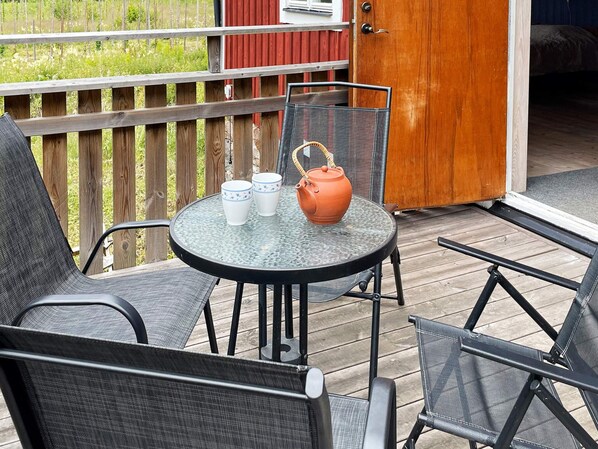 A round glass table with two white cups and an orange teapot on a wooden deck.