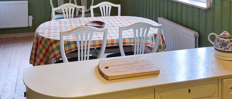 Un comedor con una mesa preparada para cuatro personas, una tabla de cortar de madera y un armario blanco con cajones.
