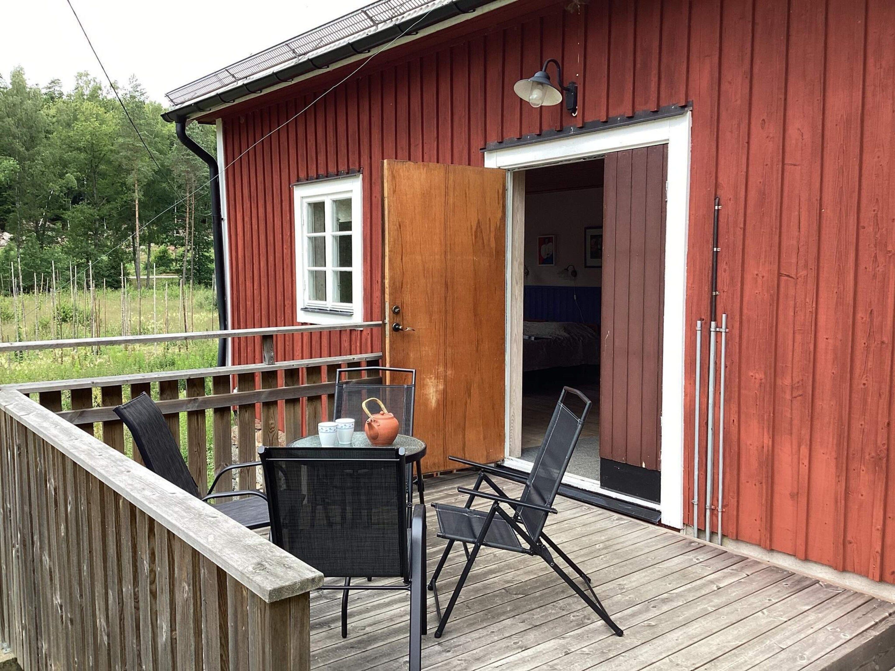 A red wooden building with a deck, a table with chairs, and a door leading to a room.