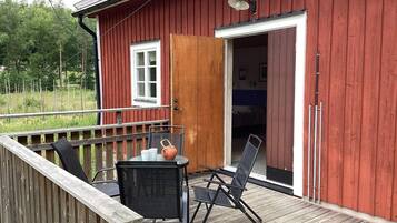 A red wooden building with a deck, a table with chairs, and a door leading to a room.