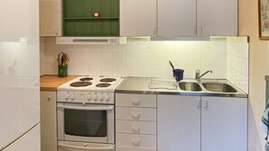 Eine kleine Küche mit weißen Schränken, einem Herd, einem Backofen und einem Spülbecken.