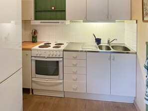 A compact kitchen with white cabinets, a stove, oven, and a sink. - 4 Star Holiday Home in Svangsta (Svangsta)