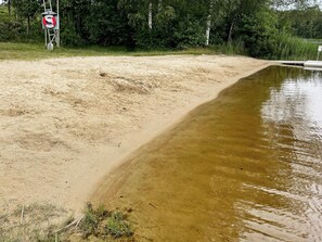 Una playa arenosa con un cuerpo de agua, un flotador salvavidas y un cartel de prohibido bañarse.
