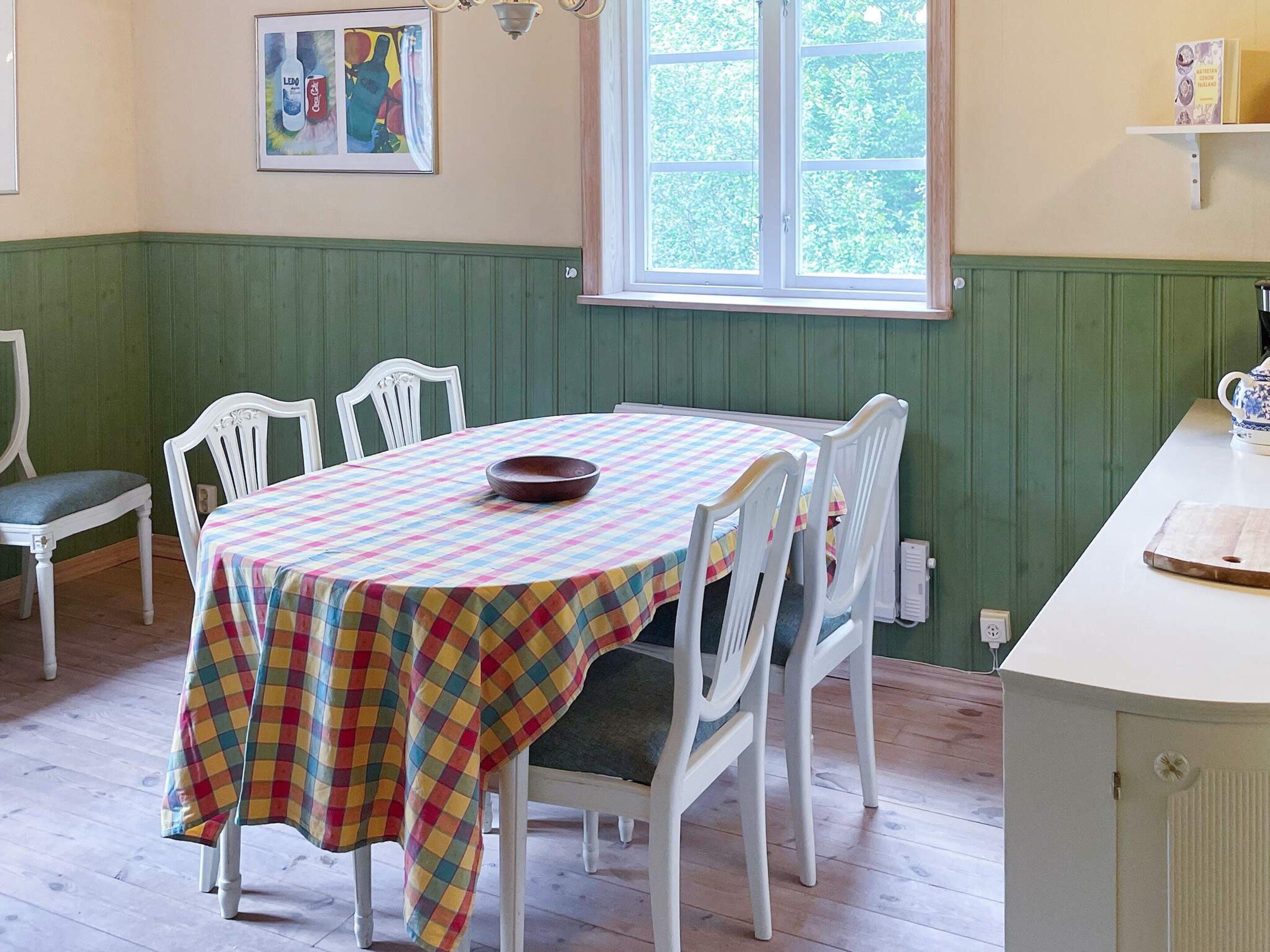 A dining area with a table covered by a colorful checkered tablecloth, surrounded by white chairs.