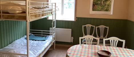 Et værelse med køjesenge, et bord med ternet dug, hvide stole og en lysekrone.