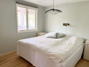 Ett sovrum med en säng, ett fönster, ett sängbord och en väggmonterad lampa.