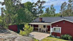 Une maison rouge avec un patio couvert, une cheminée et une vue sur une zone boisée.