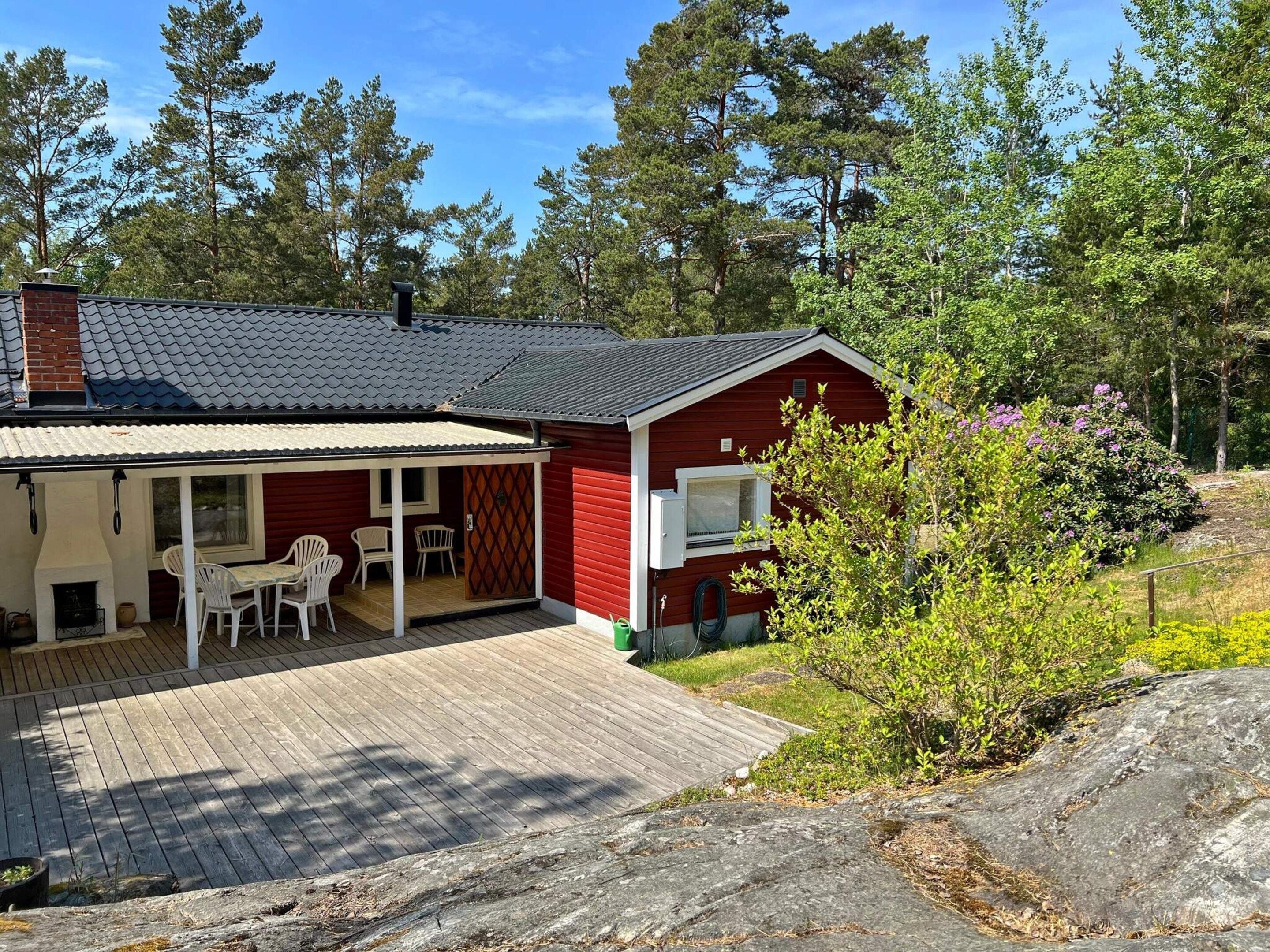 A red cabin with a covered patio, outdoor seating, and a view of a forested area.