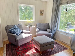 A room with two grey armchairs, a small table, a red patterned rug, and a window with a view of greenery. - 6 Person Holiday Home in Djurhamn (Fågelbrolandet)