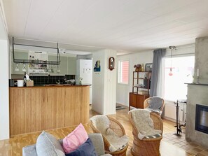 Ein Wohnzimmer mit Holzbalken, Korbstühlen, einem Kamin und einer Küche im Hintergrund.