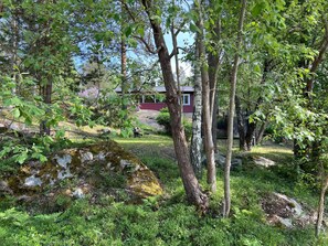 Un paysage naturel avec un bâtiment rouge, des arbres et un rocher recouvert de mousse.