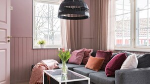 Ein gemütliches Wohnzimmer mit grauem Sofa, einem Glastisch und einer schwarzen gewebten Pendelleuchte.