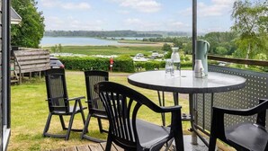 Eine Terrasse mit einem runden Tisch und vier Stühlen mit Blick auf einen See und Felder.