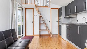 Eine moderne Wohnung mit einer Holztreppe, einem schwarzen Ledersofa und einer Küche mit grauen Schränken.
