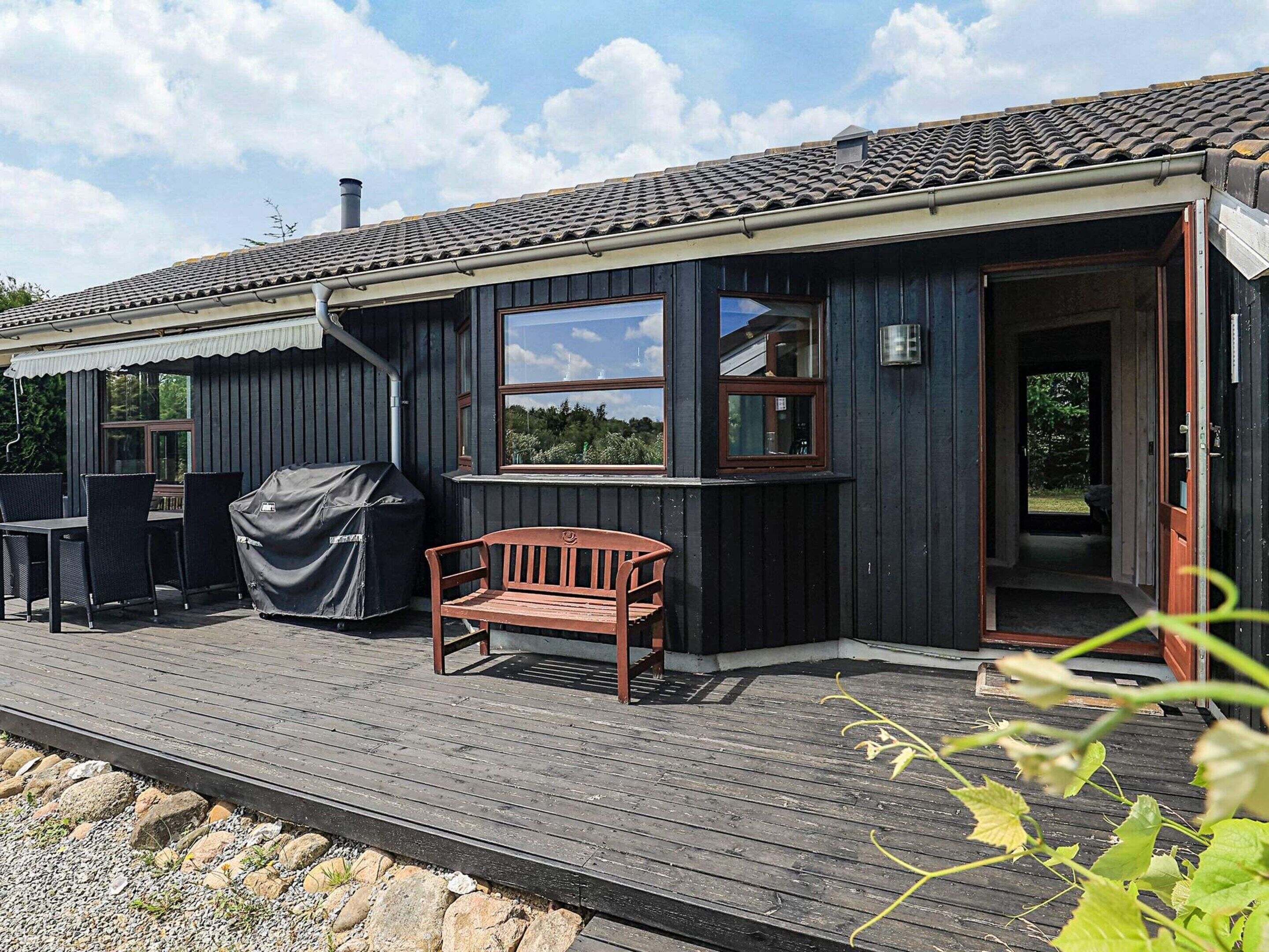 A wooden cabin with a deck, a covered grill, and a bench.