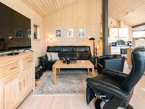 A cozy cabin interior with a wooden interior, a leather sofa, a dining table, and a kitchen area.