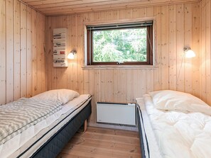 A small, cozy room with two beds, a window with a view of greenery, and a wall-mounted power outlet with a lamp.