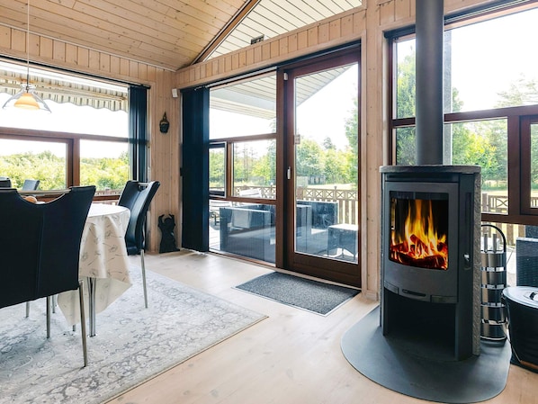 A cozy room with a wood-burning stove, large windows, and a dining area. - 4 Star Holiday Home in Oster Assels (Øster Assels)