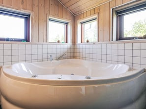 Ett badrum med ett stort badkar, träpanel på väggarna och kakelgolv.
