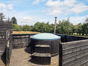 Ein Whirlpool mit einer Holzterrasse und Blick auf Bäume und Himmel.