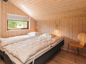 Ein Schlafzimmer mit Holzboden, einem Bett mit weißer Bettwäsche, einem Fenster mit Jalousien und einem Sessel.