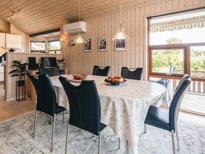 A dining area with a round table, black chairs, and a white tablecloth. There are two pendant lights, a wall-mounted air conditioner, and framed artwork on the wall. - 4 Star Holiday Home in Oster Assels (Øster Assels)