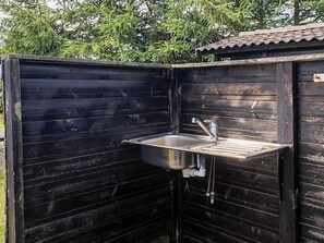Un petit espace de cuisine extérieur, avec un évier et un robinet en métal, entouré de murs en bois.