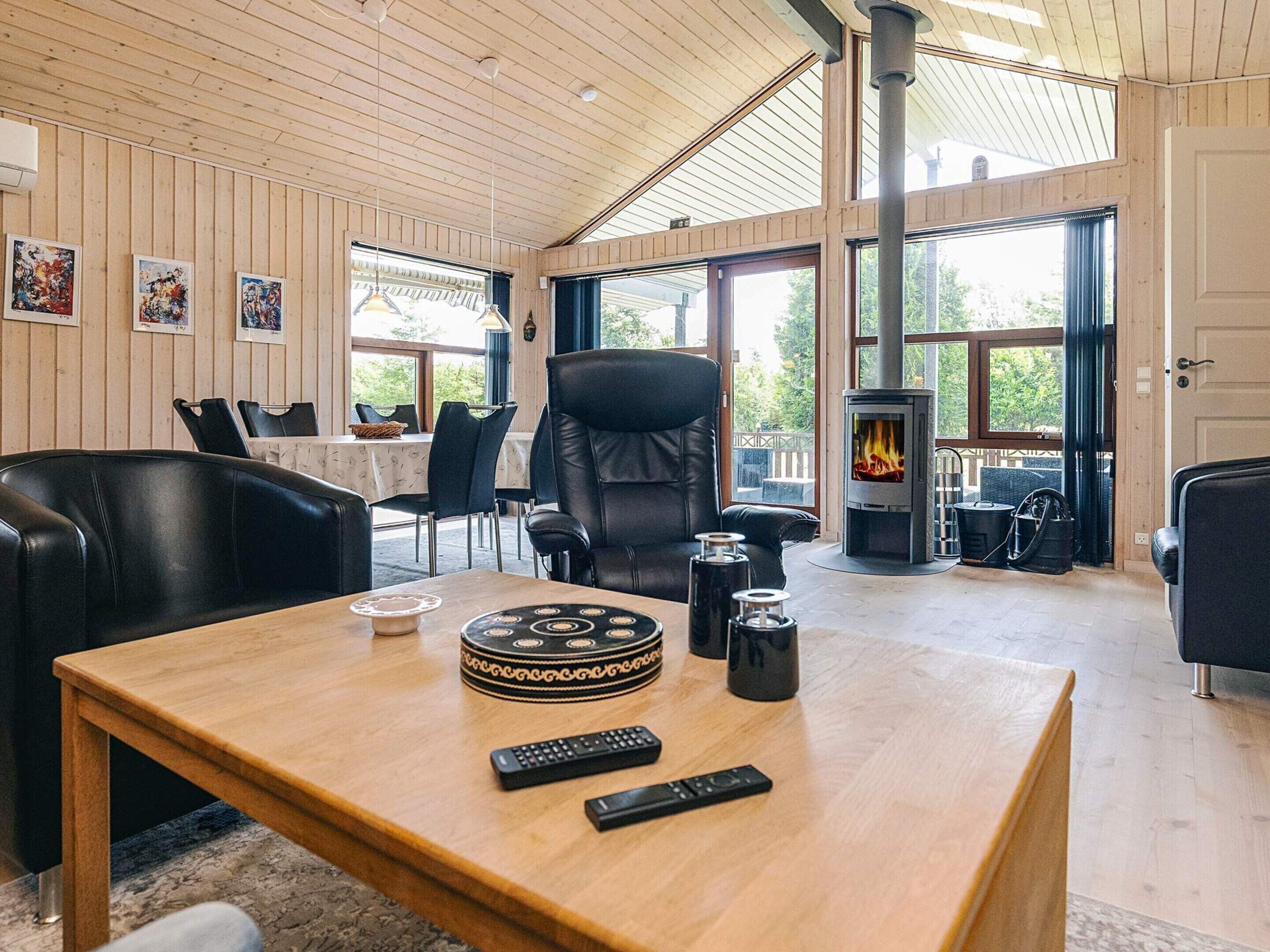 A cozy living room with a fireplace, leather chairs, a wooden table with a coffee pot, and a TV remote.