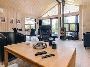 Un salon chaleureux avec une cheminée, des fauteuils en cuir, une table en bois sur laquelle se trouve une cafetière et une télécommande.