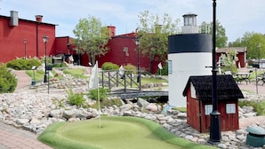 A miniature golf course with a red building, a black and white lighthouse, and a small wooden structure. - 4 Person Holiday Home in Hallstavik (Hallstavik)