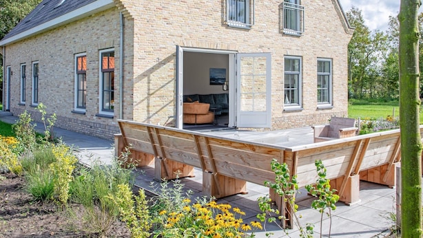 Una casa de piedra con un patio amplio y abierto, una terraza de madera y un jardín con flores amarillas.