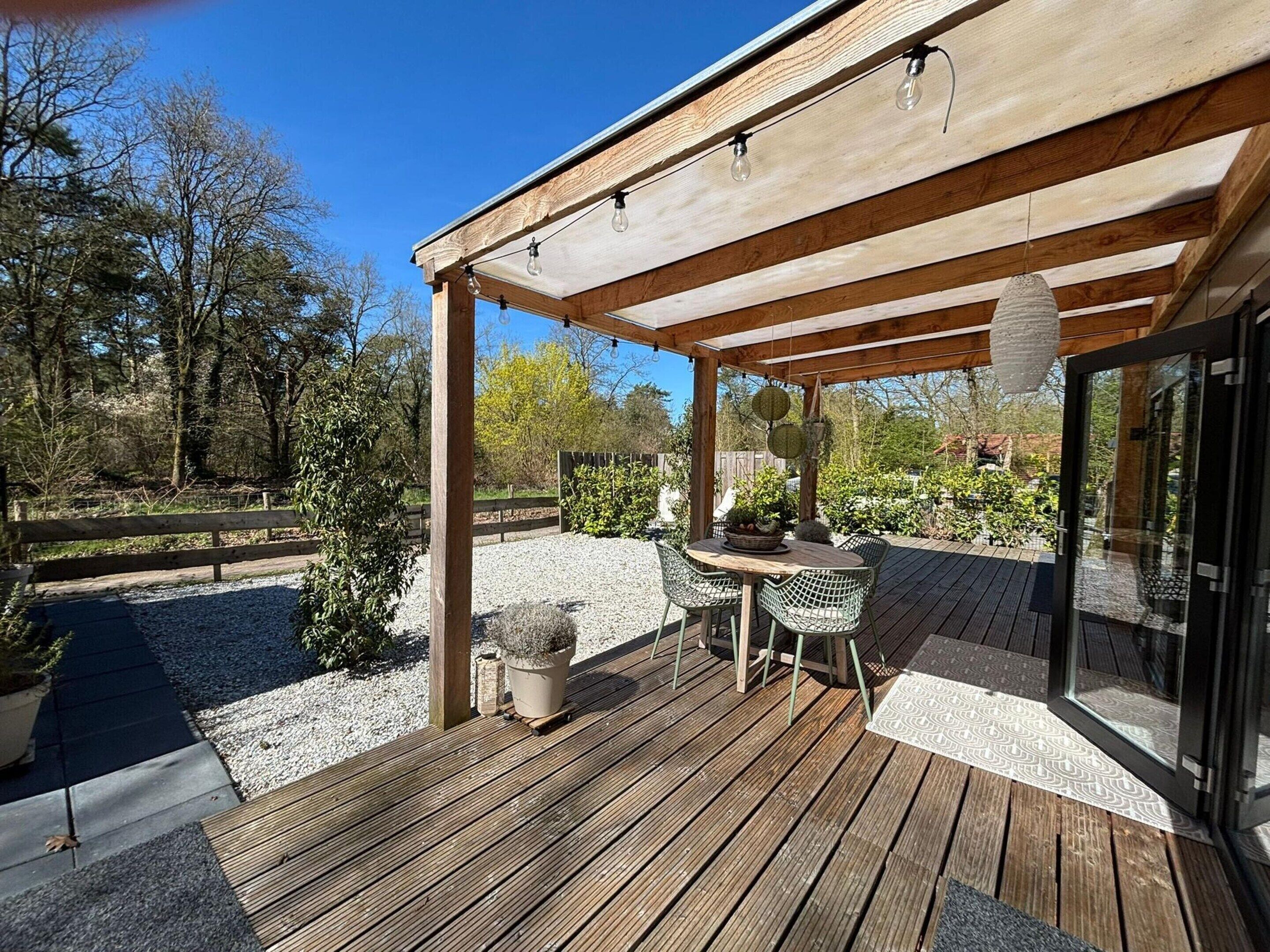 Eine überdachte Terrasse mit Holzdeck, Sitzgelegenheit im Freien und Blick auf die umliegende Landschaft.