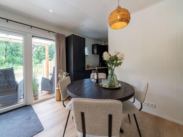 A dining area with a round table, chairs, a vase with flowers, and a hanging light fixture. - Lodge in Hattemerbroek Near Veluwe Forest (Hattemerbroek)